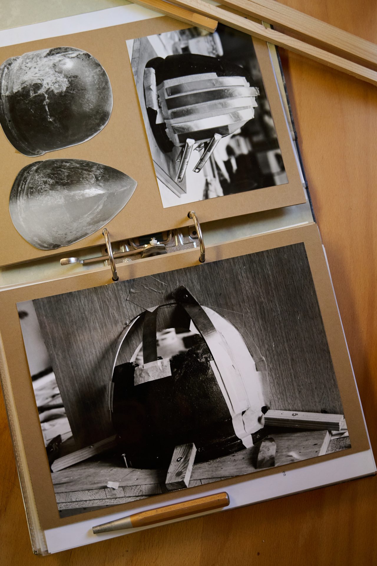 Skizzen und Fotos eines Modells oder Prototyps in einem offenen Ordner auf einem Tisch.