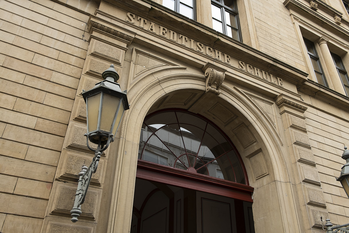 Historisches Schulgebäude mit klassischem Eingangsportal und Laterne, beschriftet "Städtische Schule".