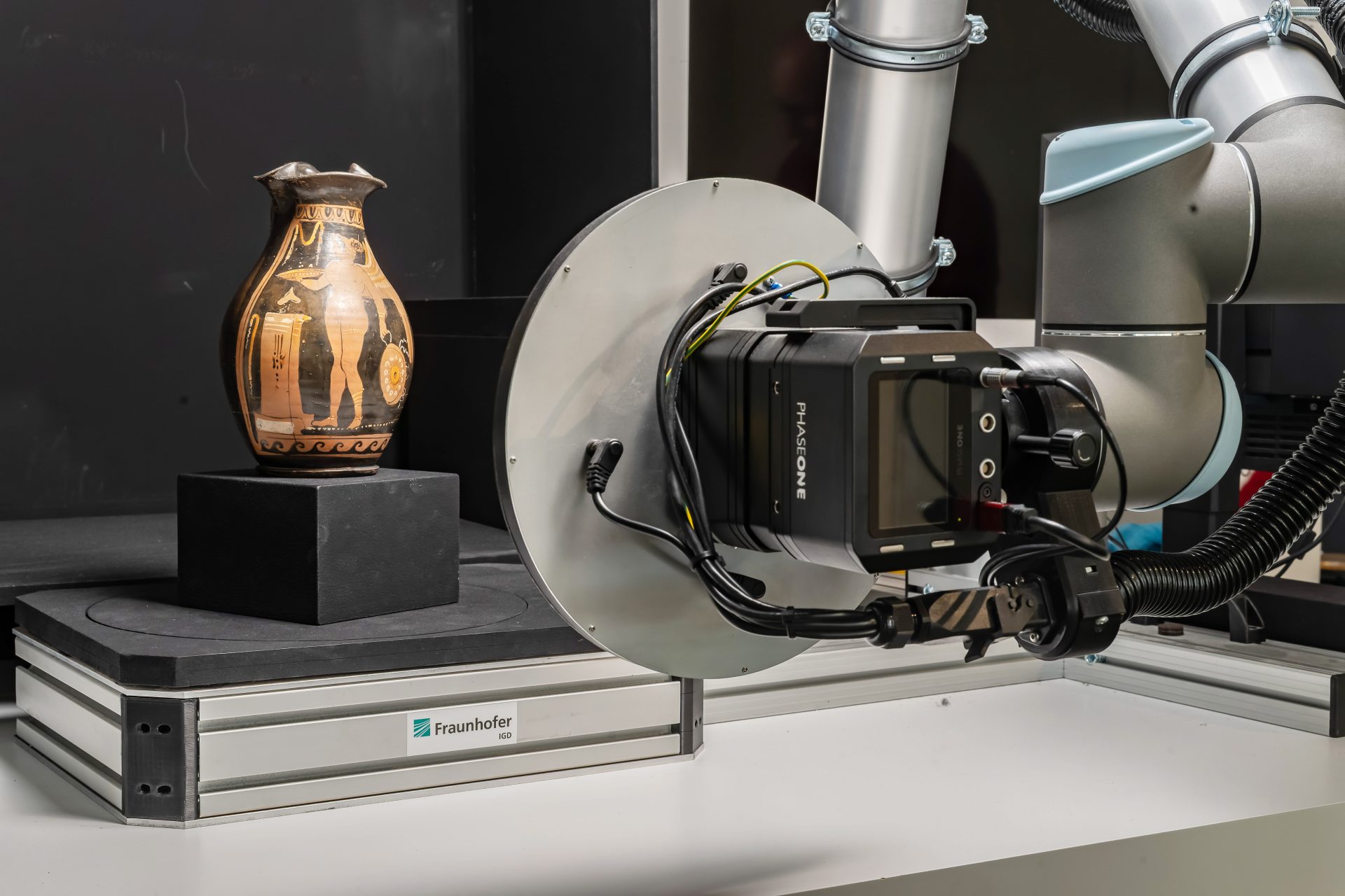 Robotikarm mit Kamera scannt antiken Krug auf einem Podest in einem Labor.