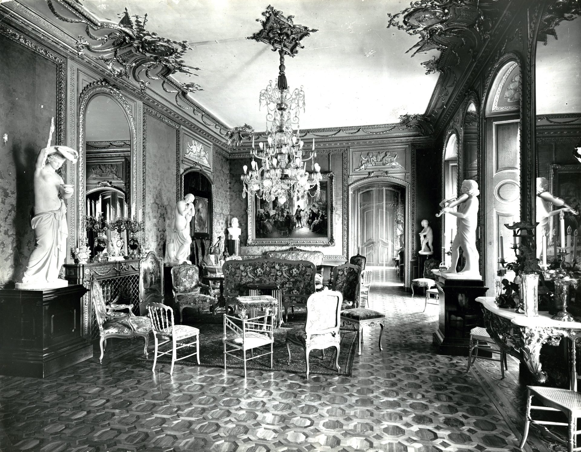 Elegantes, historisches Interieur mit Skulpturen, prunkvollen Möbeln und einem beeindruckenden Kronleuchter.