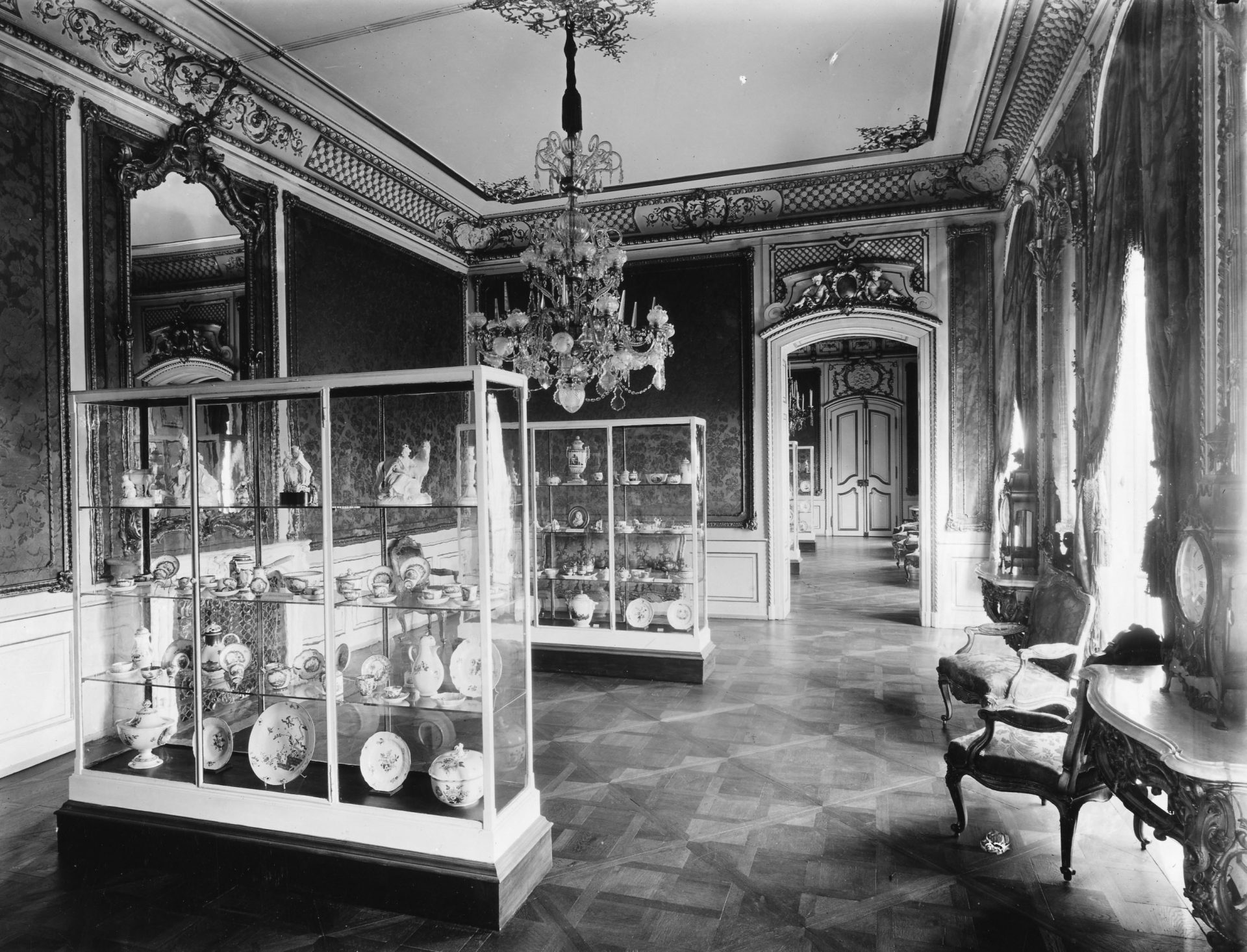 Eleganter Innenraum mit antiken Vitrinen, kostbarem Geschirr und opulenter Dekoration in Schwarz-Weiß.