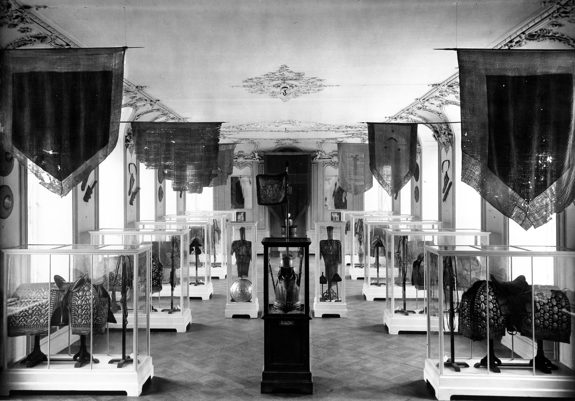Museumsausstellung mit Glasvitrinen, historischen Objekten und hängenden Bannern in einem stilvollen Raum.