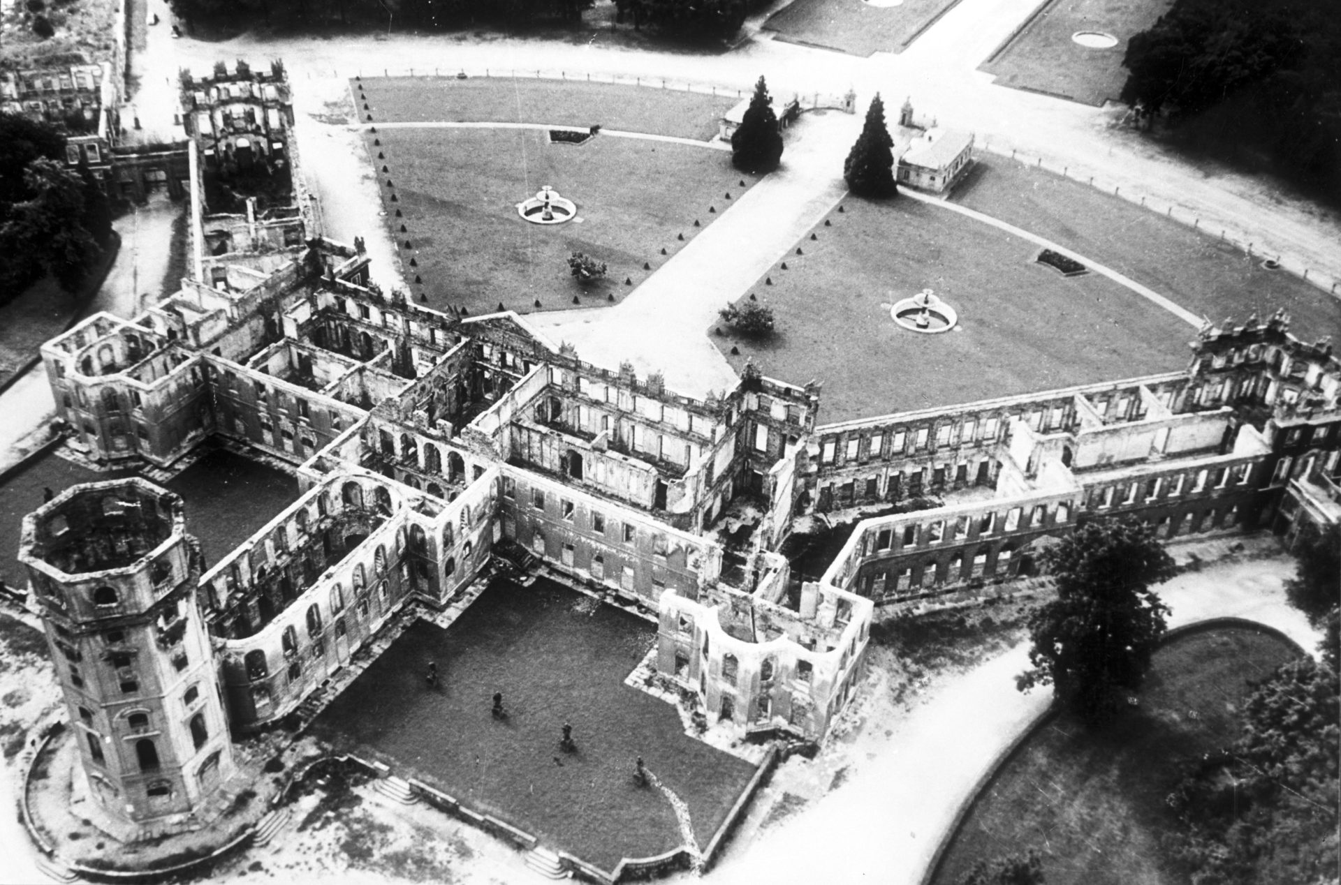 Luftaufnahme einer Ruine mit erhaltenen Mauern und einem gepflegten, symmetrischen Gartenbereich.