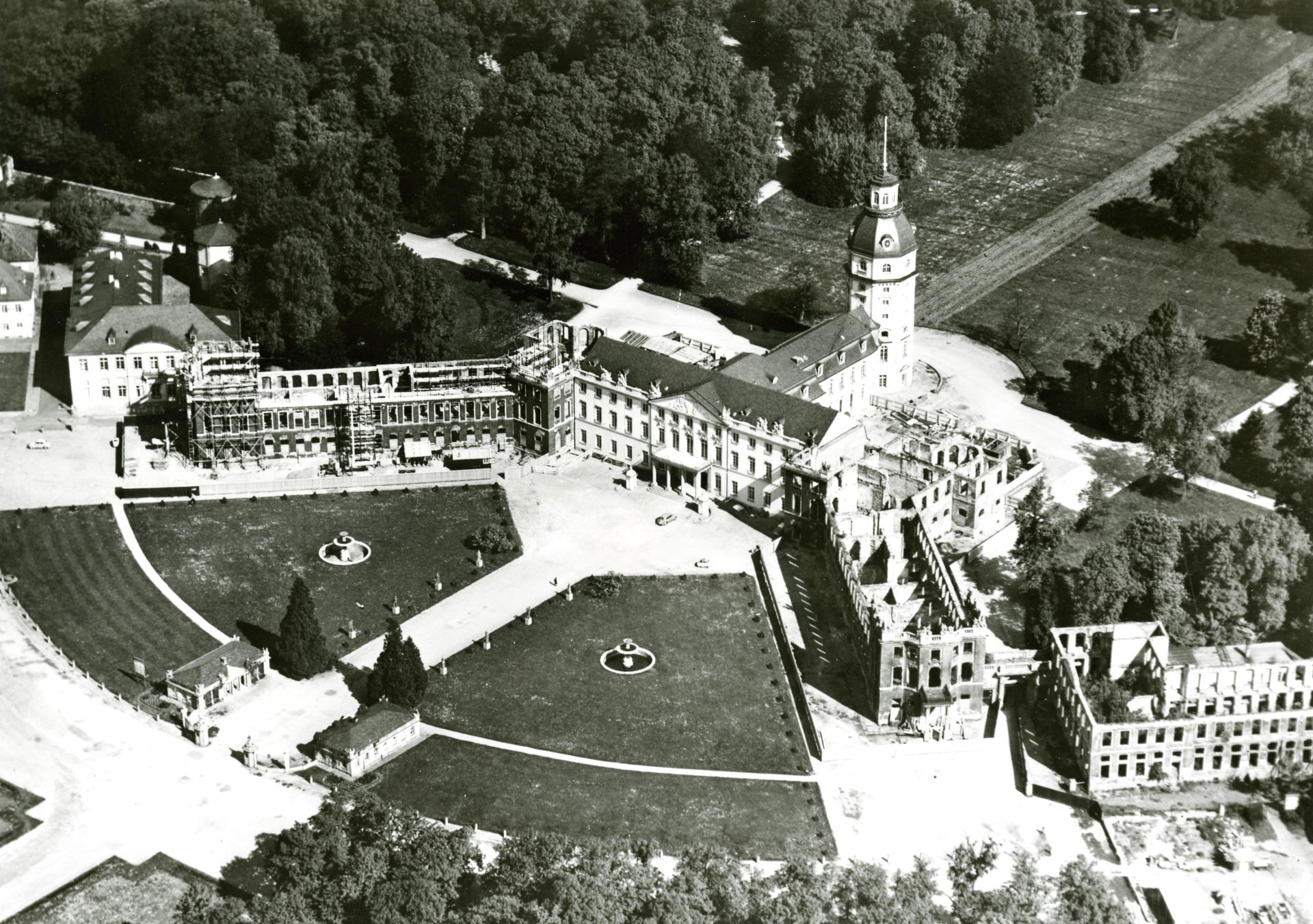 Luftaufnahme eines historischen Gebäudes mit Parkanlagen, teilweise renoviert, umgeben von Bäumen.