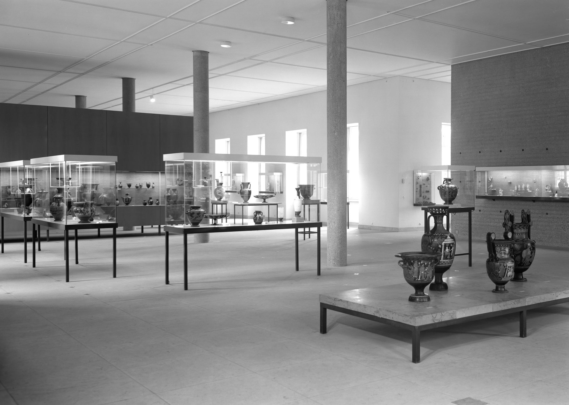 Modernes Museumsinnere mit Vitrinen und antiken Vasen in Schwarz-Weiß. Helle Räume und klare Linien.