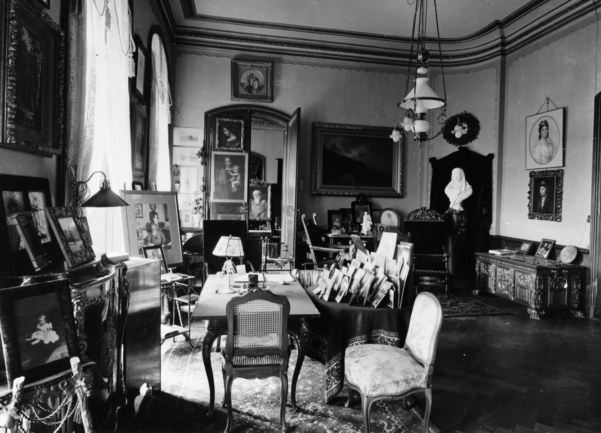 Schwarz-weiß Foto eines historischen Raumes mit Möbeln, Bildern und Dekorationen an Wänden und Tischen.