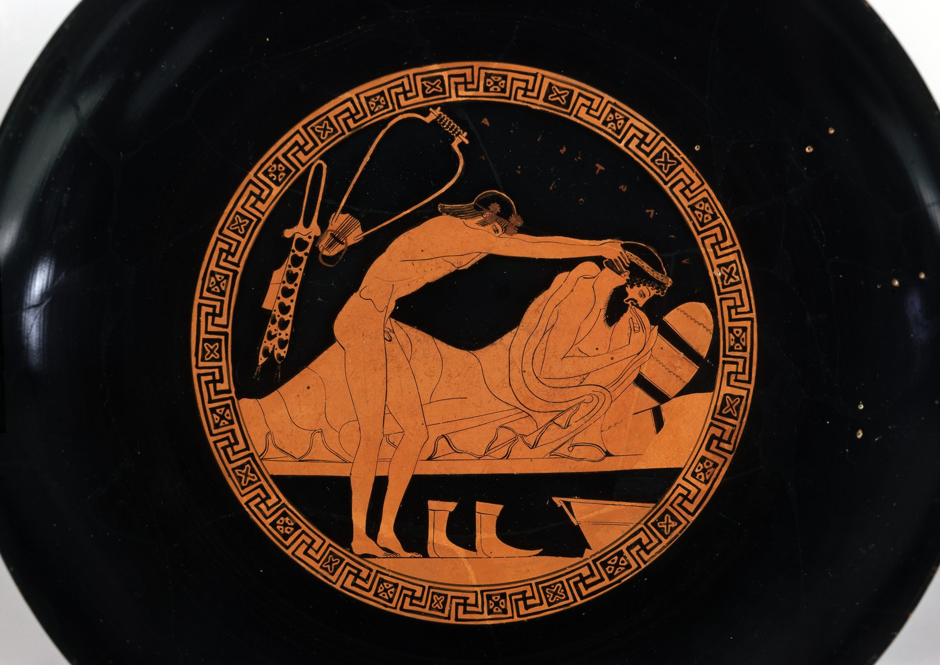 Antike griechische Vase mit Abbildungen von zwei Männern in einer intimen Szene, umgeben von ornamentalen Mustern.