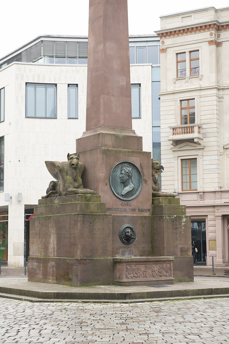 Denkmal für Carl, Großherzog von Baden, mit geflügelten Skulpturen und Bronzeplakette in städtischer Umgebung.