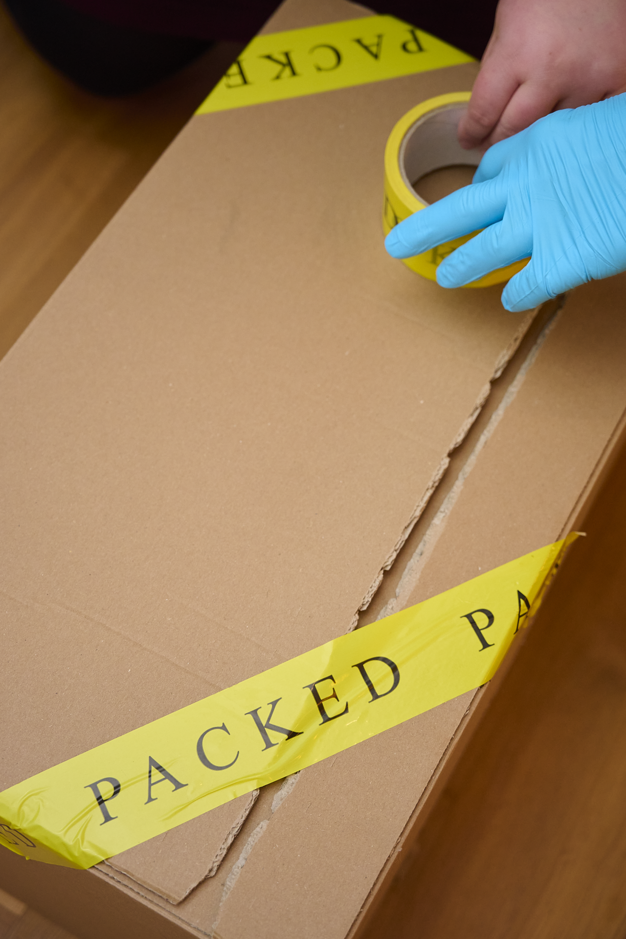 Eine Person bringt gelbes „Packed“-Klebeband auf einem Karton an, um ihn zu verschließen.