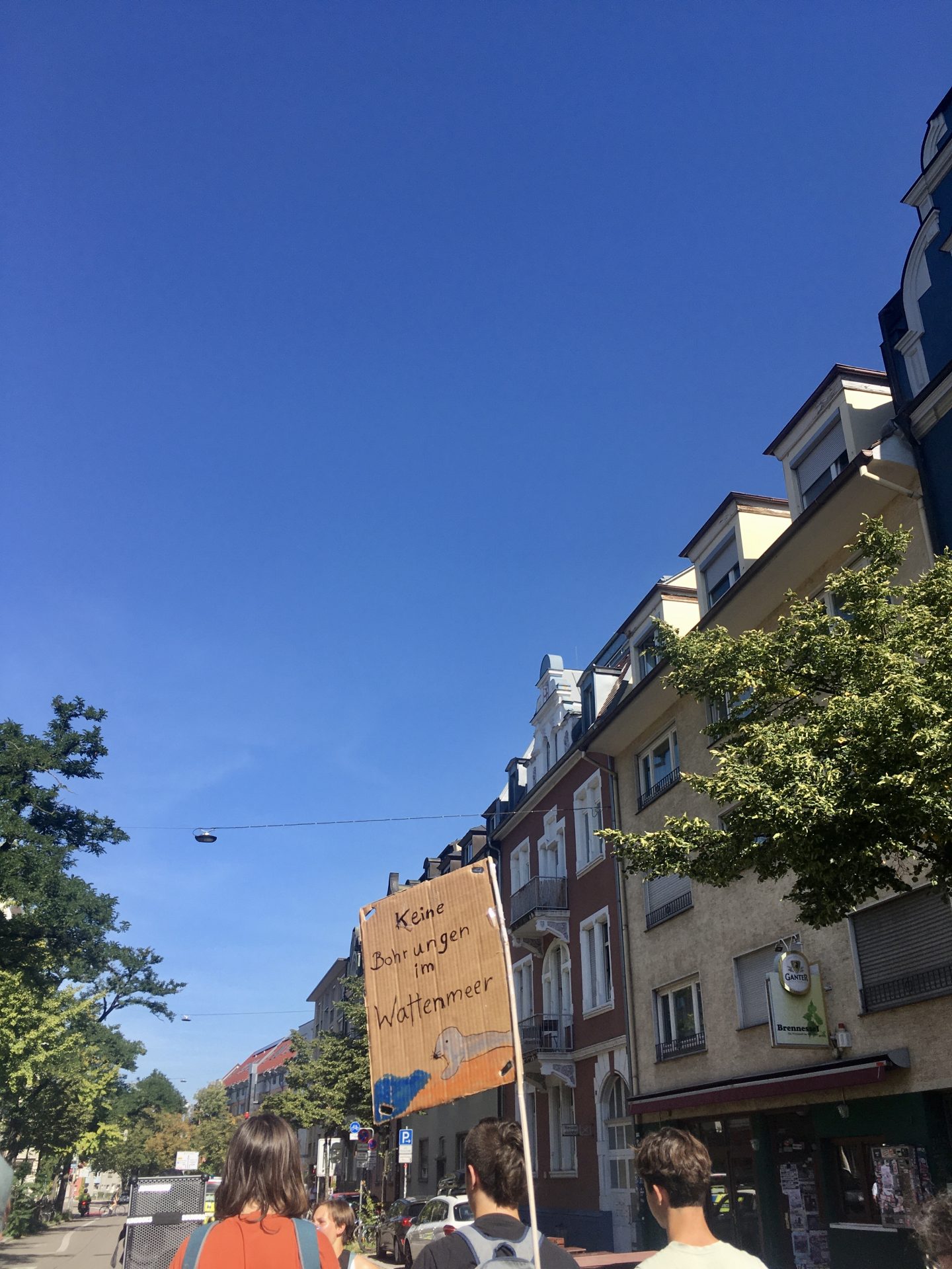 Demonstrierende Personen halten ein Schild mit „Keine Bohrungen im Wattenmeer“ vor einer städtischen Kulisse hoch.