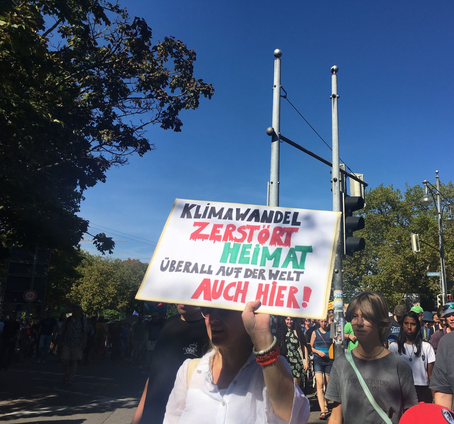 Teilnehmer einer Demonstration halten ein Schild, das sagt: „Klimawandel zerstört Heimat – Auch hier!“