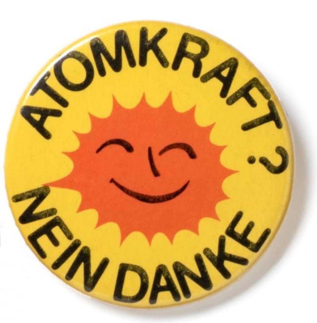 Gelbes Abzeichen mit lächelnder Sonne und dem Text: "ATOMKRAFT? NEIN DANKE".