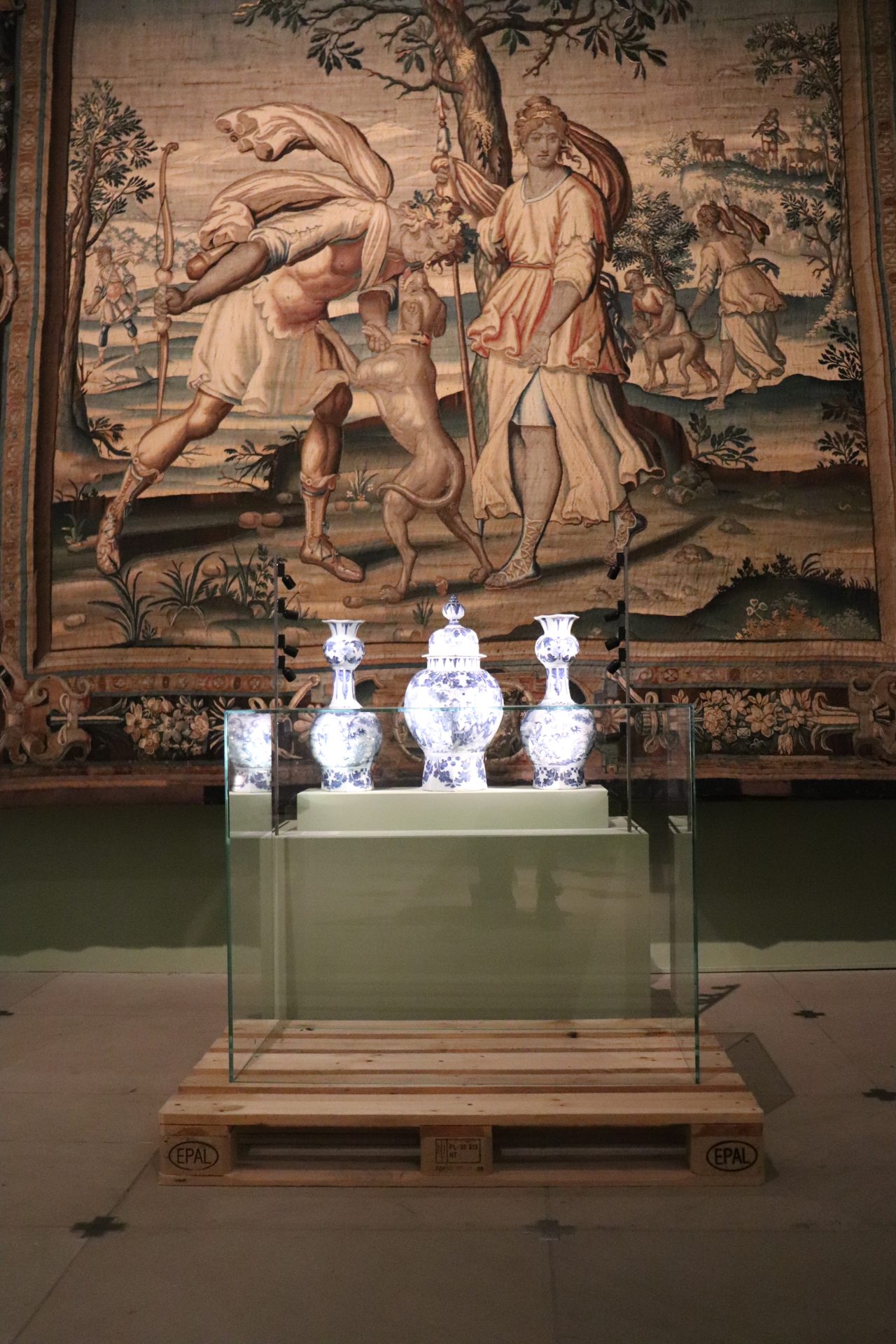 Eine Ausstellung im Abbau. Im Vordergrunde eine Vitrine mit drei Porzelanvasen, die Glashaube steht auf einer Palette davor.