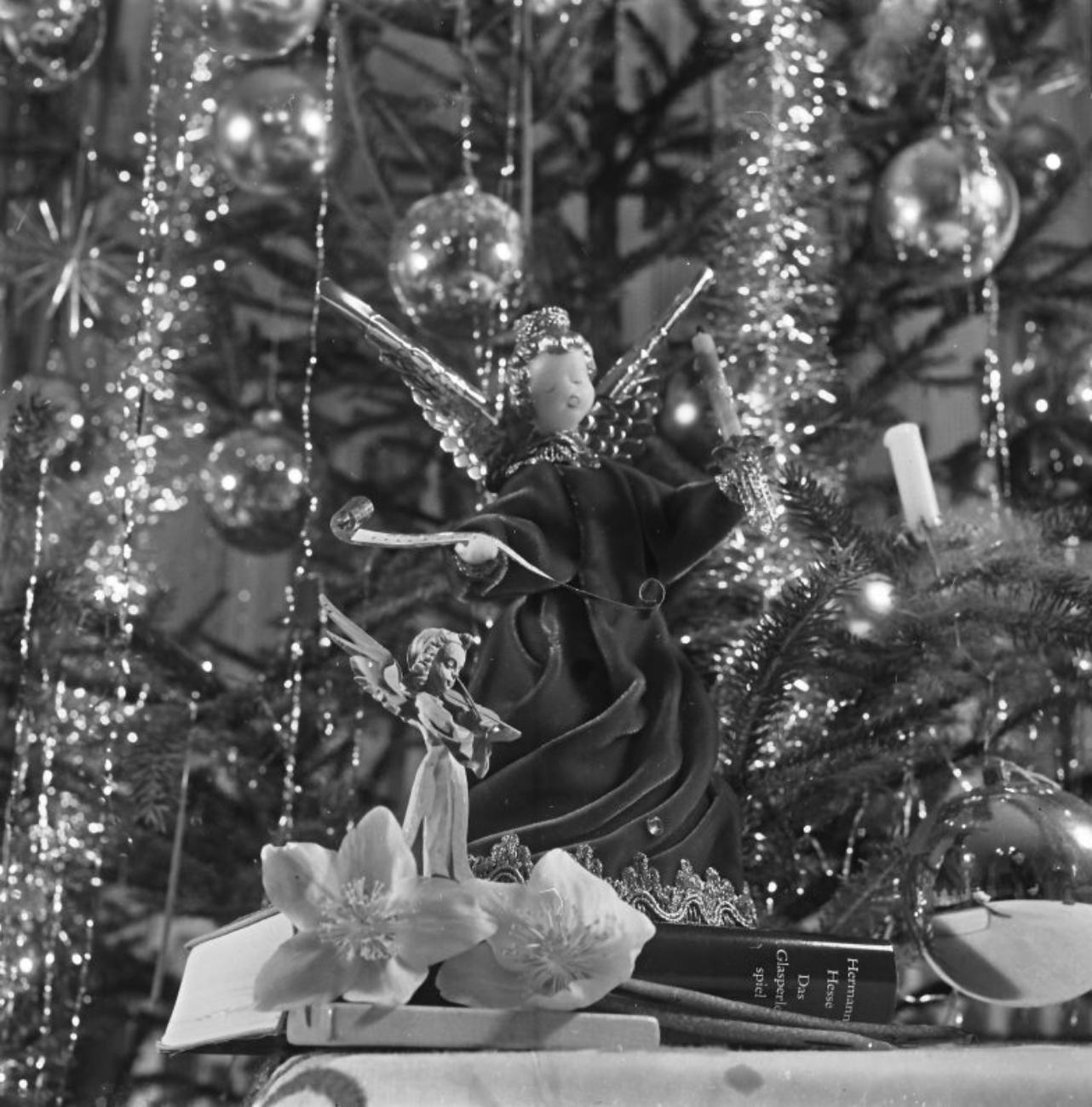 Schwarz-weißes Bild eines Weihnachtsbaums mit Engel-Statuen, Büchern und Blumen als dekorativen Elementen.