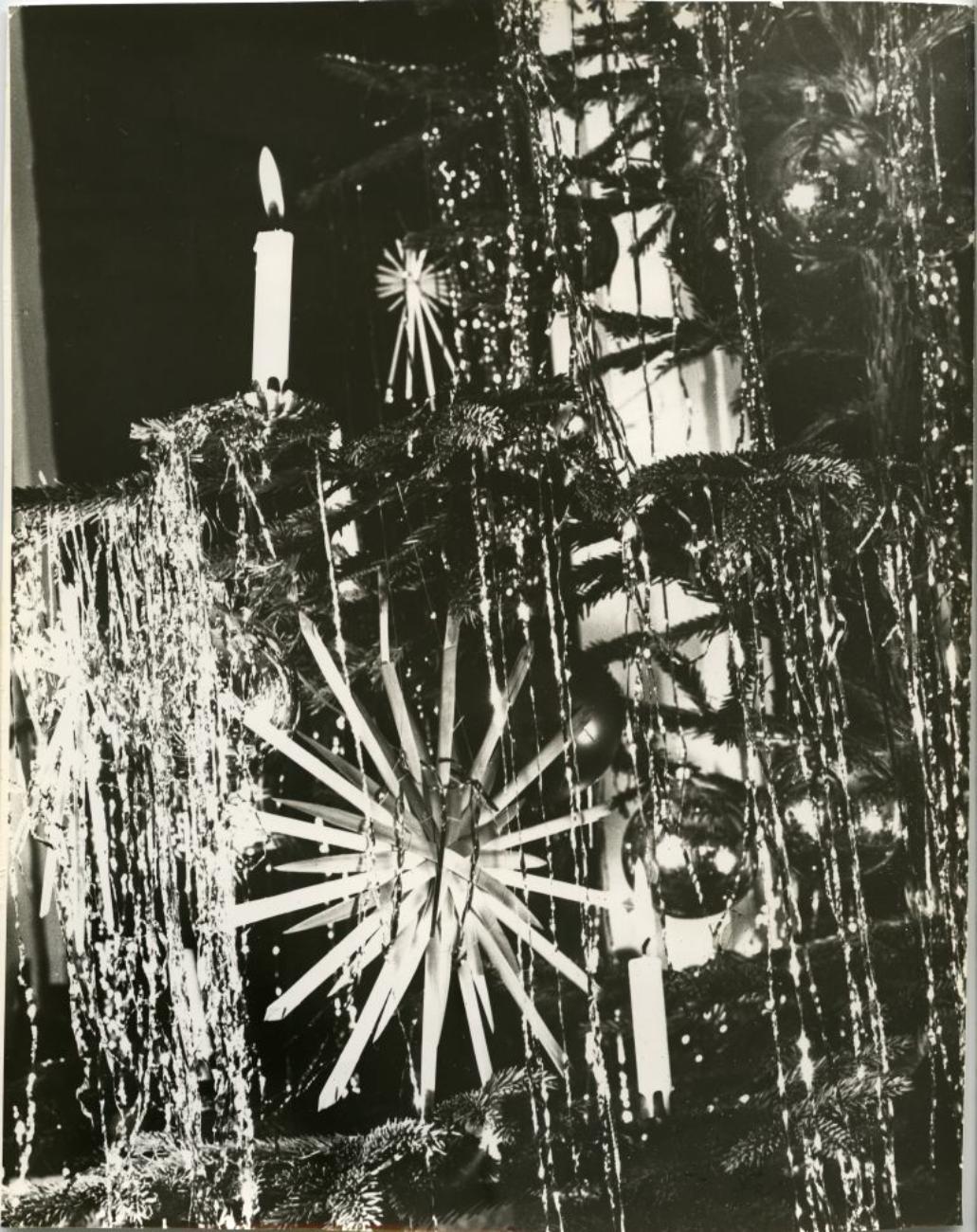 Schwarz-weiß-Bild eines festlich geschmückten Weihnachtsbaums mit Kerzen, Glitzer und einem dekorativen Stern.