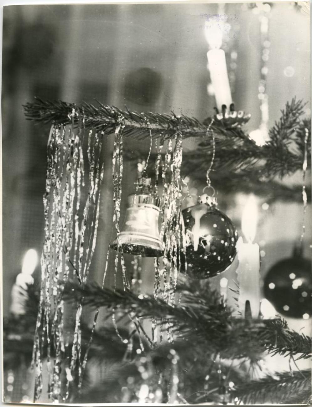 Schwarz-weißes Bild eines festlich geschmückten Weihnachtsbaums mit Glocke, Kugeln und Kerzen im Hintergrund.