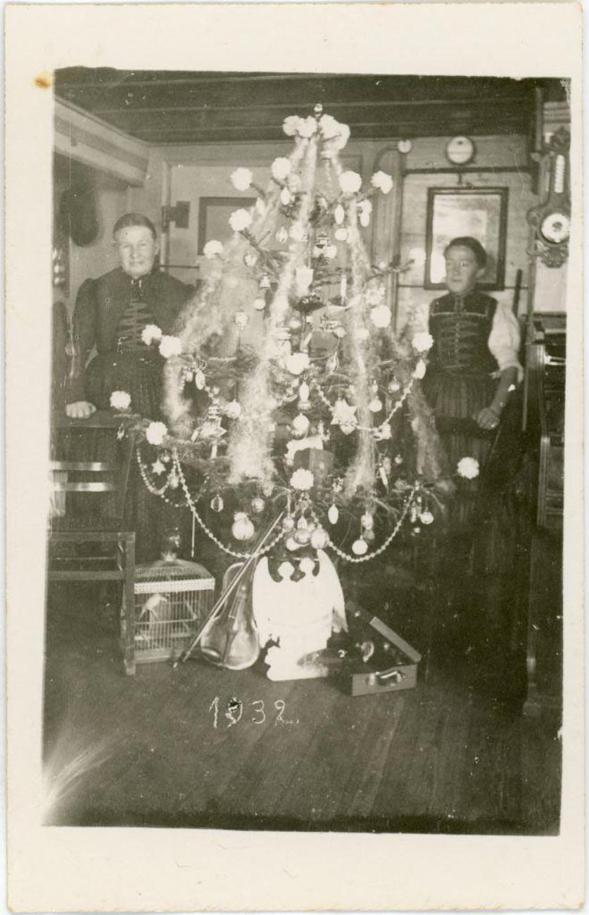 Historisches Foto von zwei Personen vor einem festlich geschmückten Weihnachtsbaum aus dem Jahr 1932.
