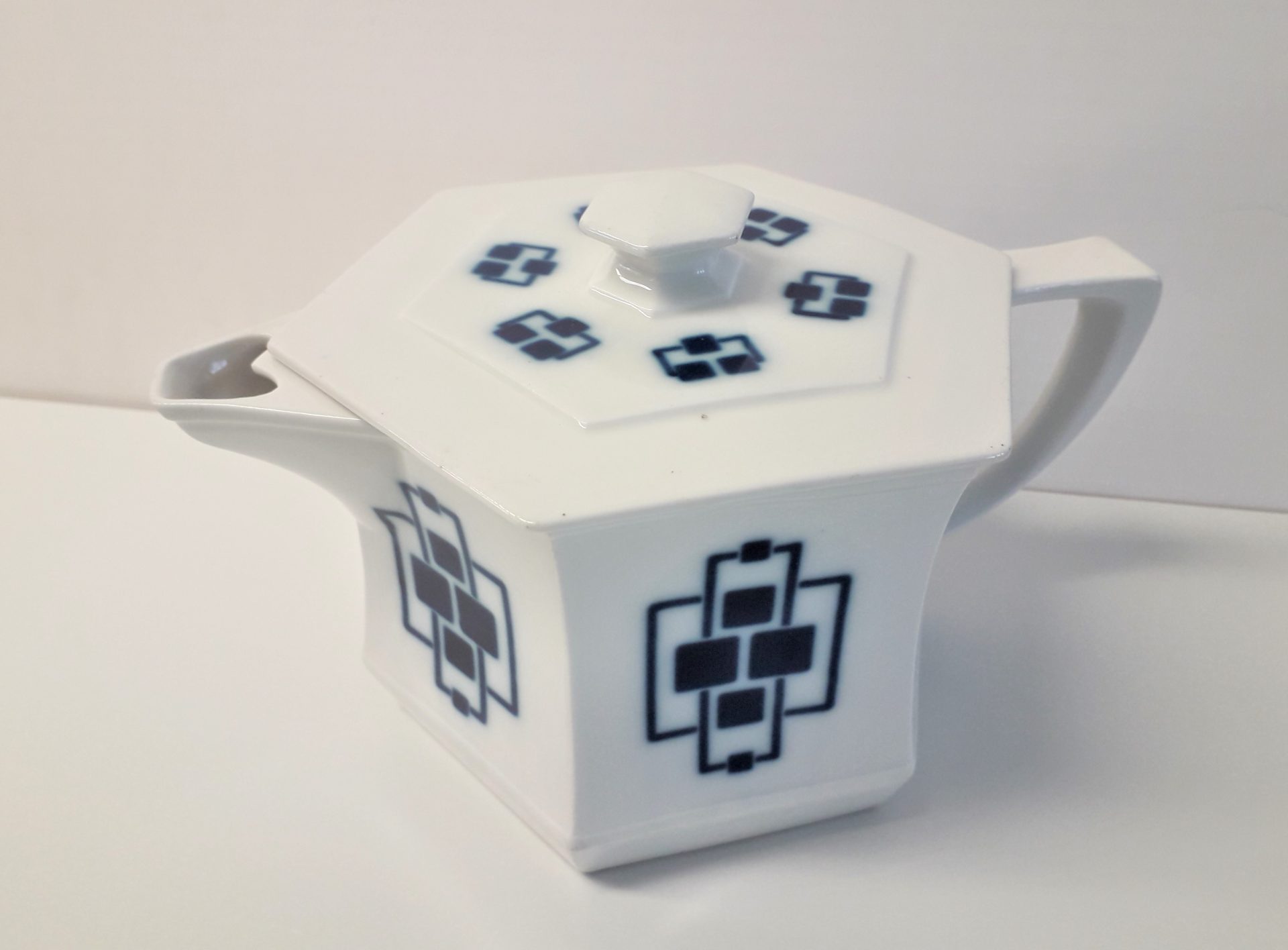 Dekorative, weiße Teekanne mit sechseckigem Deckel und schwarzem Design. Stilvolles Geschirr für Teeliebhaber.