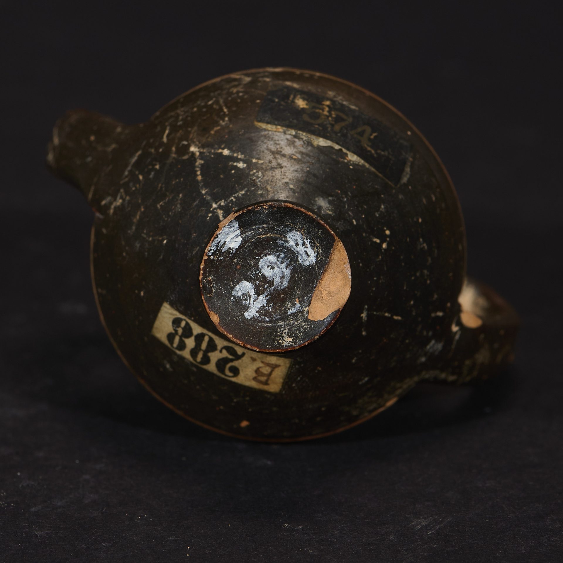 Schwarze, antike Tonkrugunterseite mit sichtbaren Zahlen und Etiketten.