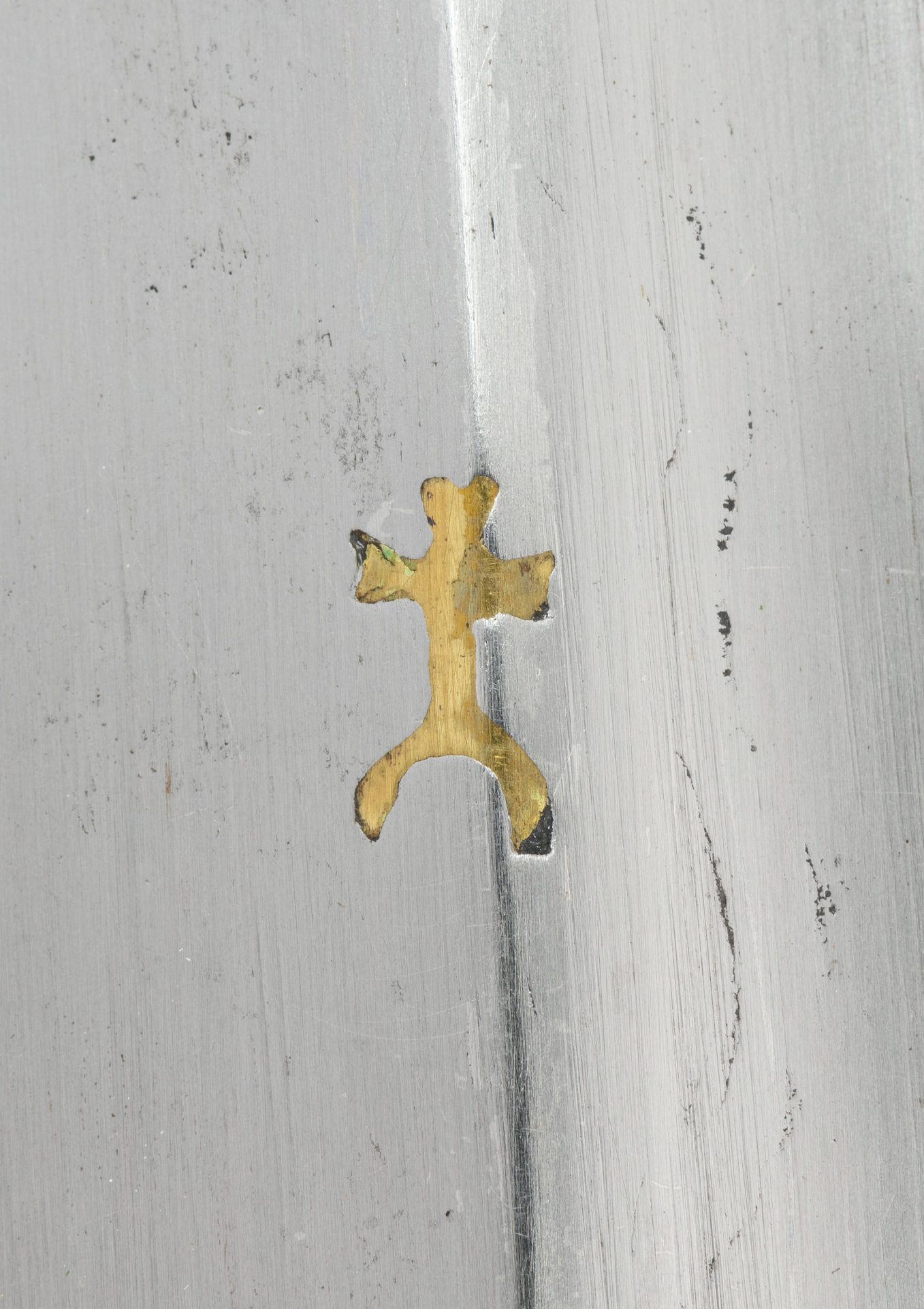 Goldene Silhouette einer Eidechse auf einer grauen, metallischen Oberfläche.