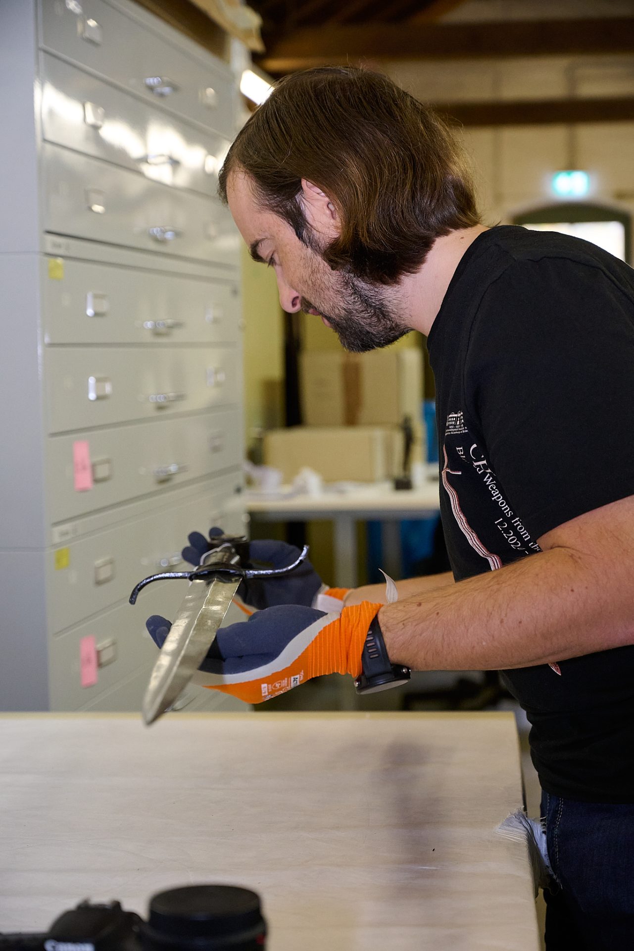 Ein Mann prüft sorgfältig eine Klinge in einem Arbeitsbereich, umgeben von Schubladenschränken.