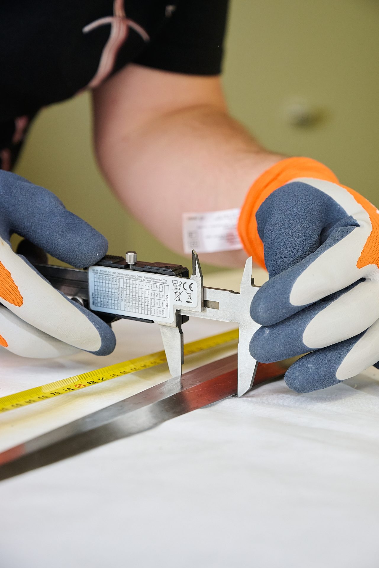 Person misst ein Metallstück mit einer Schieblehre und nutzt gleichzeitig einen Zollstock.