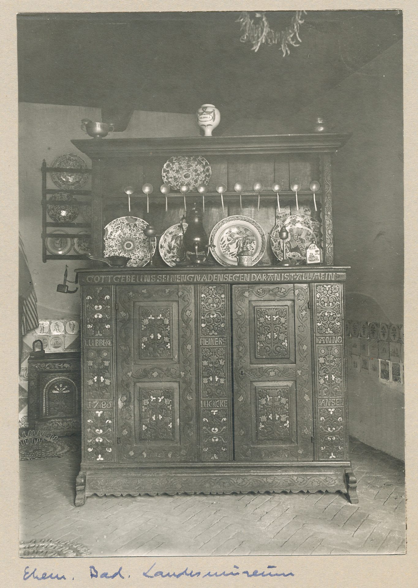 Historischer Holzschrank mit kunstvollen Verzierungen und Geschirr, umgeben von traditioneller Wohnraumatmosphäre.