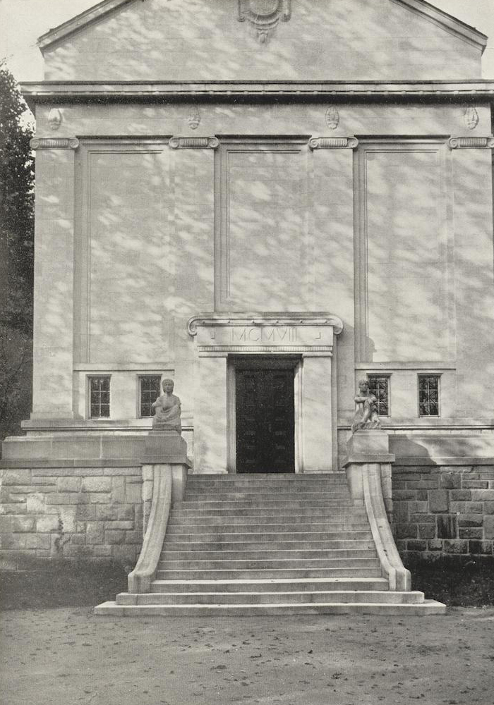Historisches Gebäude mit Treppe, Statuen auf Podesten und Fenstern im Schatten der Bäume.