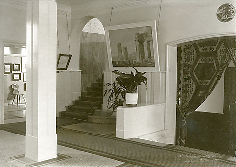 Historische Innenszene mit Treppe, Pflanzen und Gemälden in einem hellen, eleganten Raum.