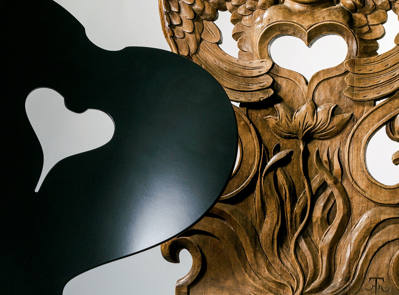 Zwei Kunstwerke: Ein glattes, schwarzes Herz und ein filigran geschnitztes, braunes Herz mit floralen Motiven.