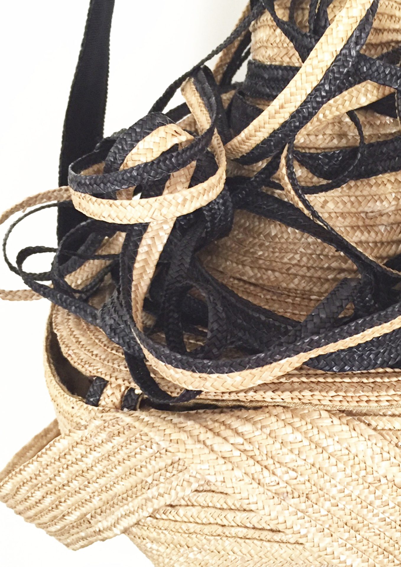 Nahaufnahme einer geflochtenen Tasche mit schwarzen und naturfarbenen Riemen, die miteinander verwoben sind.