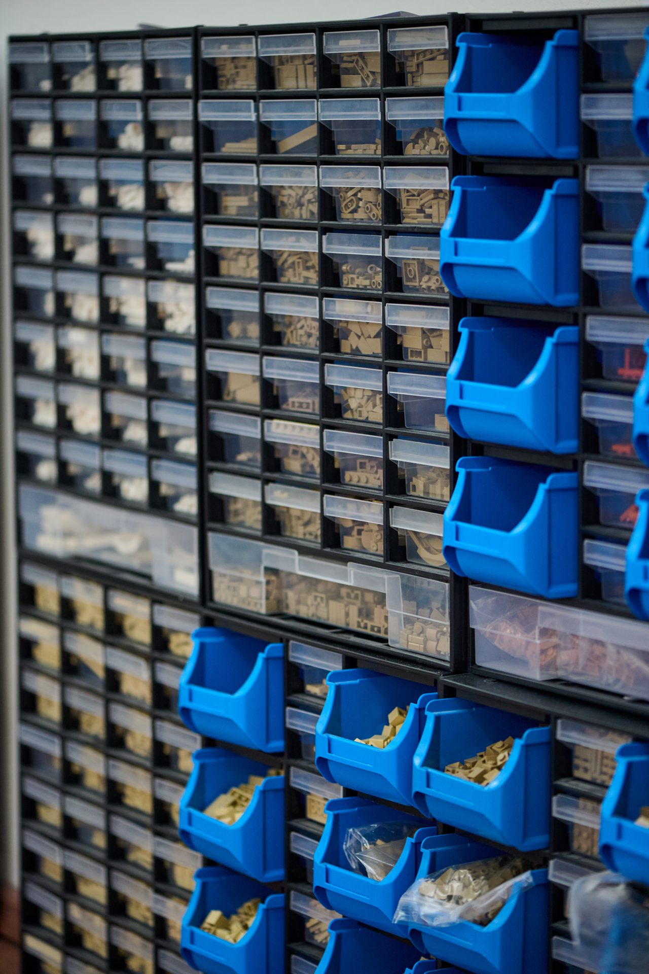 Wandregal mit transparenten und blauen Behältern, gefüllt mit Bauteilen und Kleinteilen zur besseren Organisation.